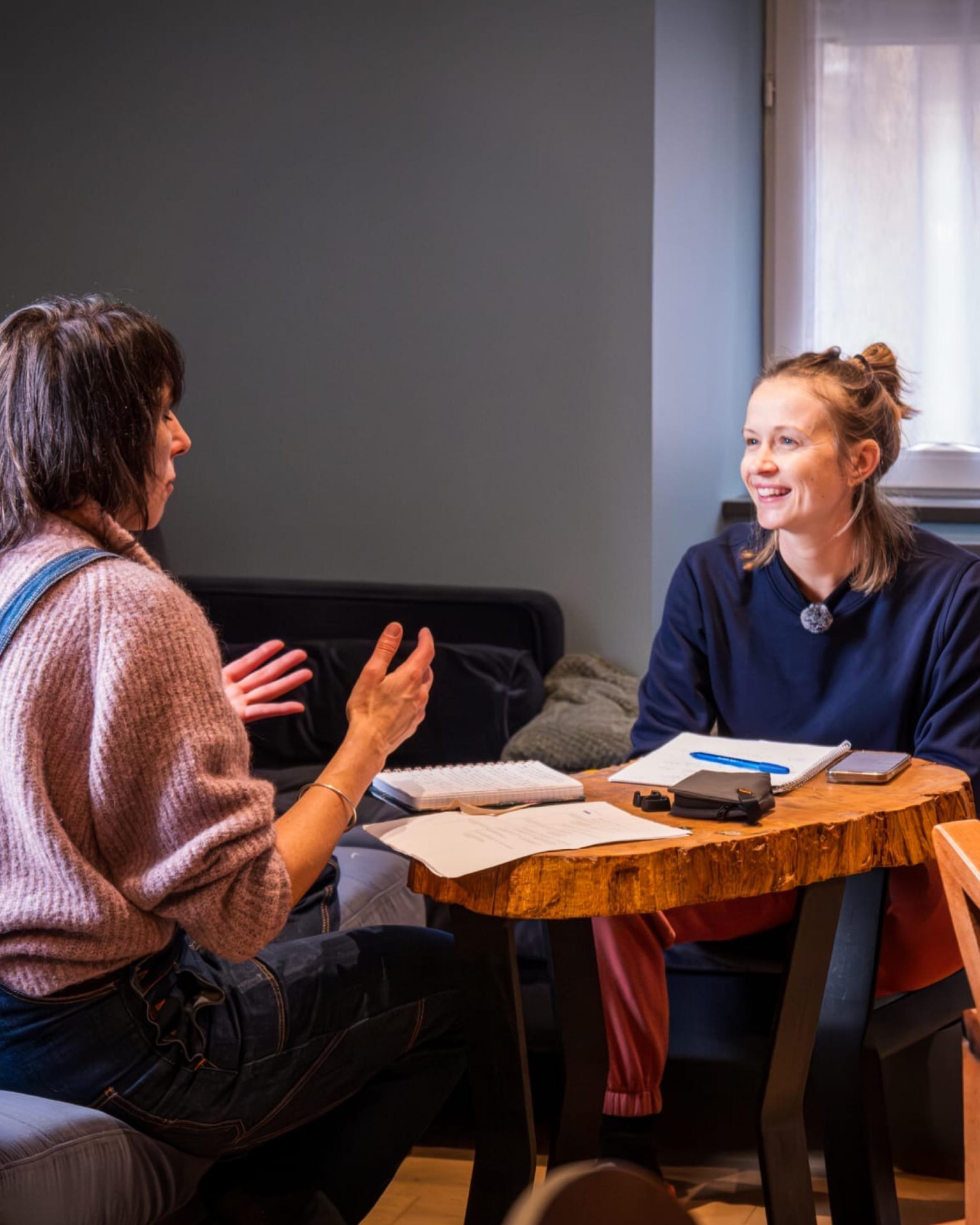 Nina Barrera en pleine discussion avec son invitée autour d'une table en bois brut couverte de carnets